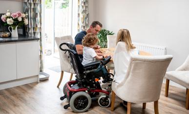 Un père et une mère sont à table en train d'aider leur enfant dans un fauteuil roulant à faire un puzzle